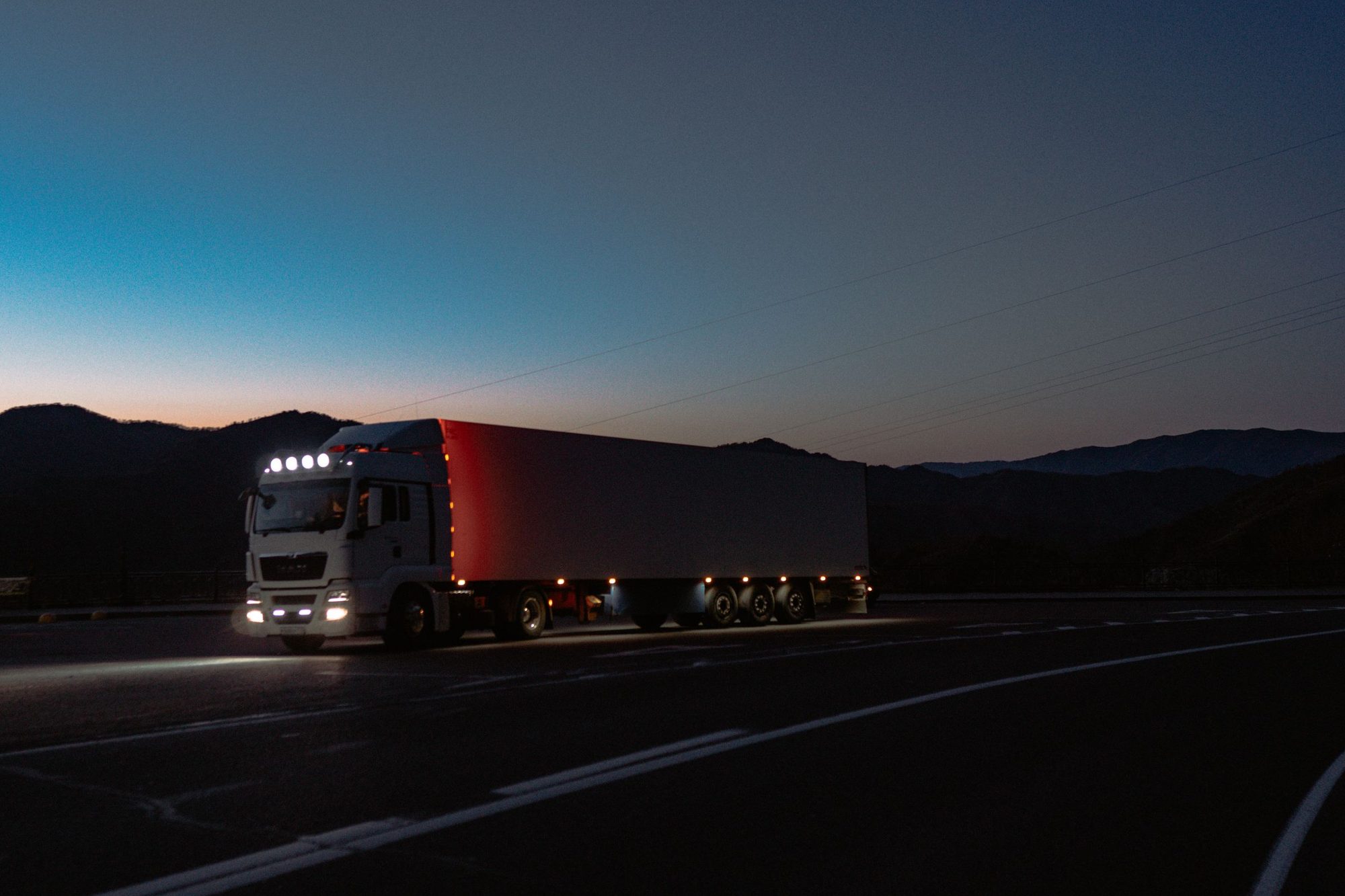 A white semi truck with a box trailer on a mountain highway at dusk