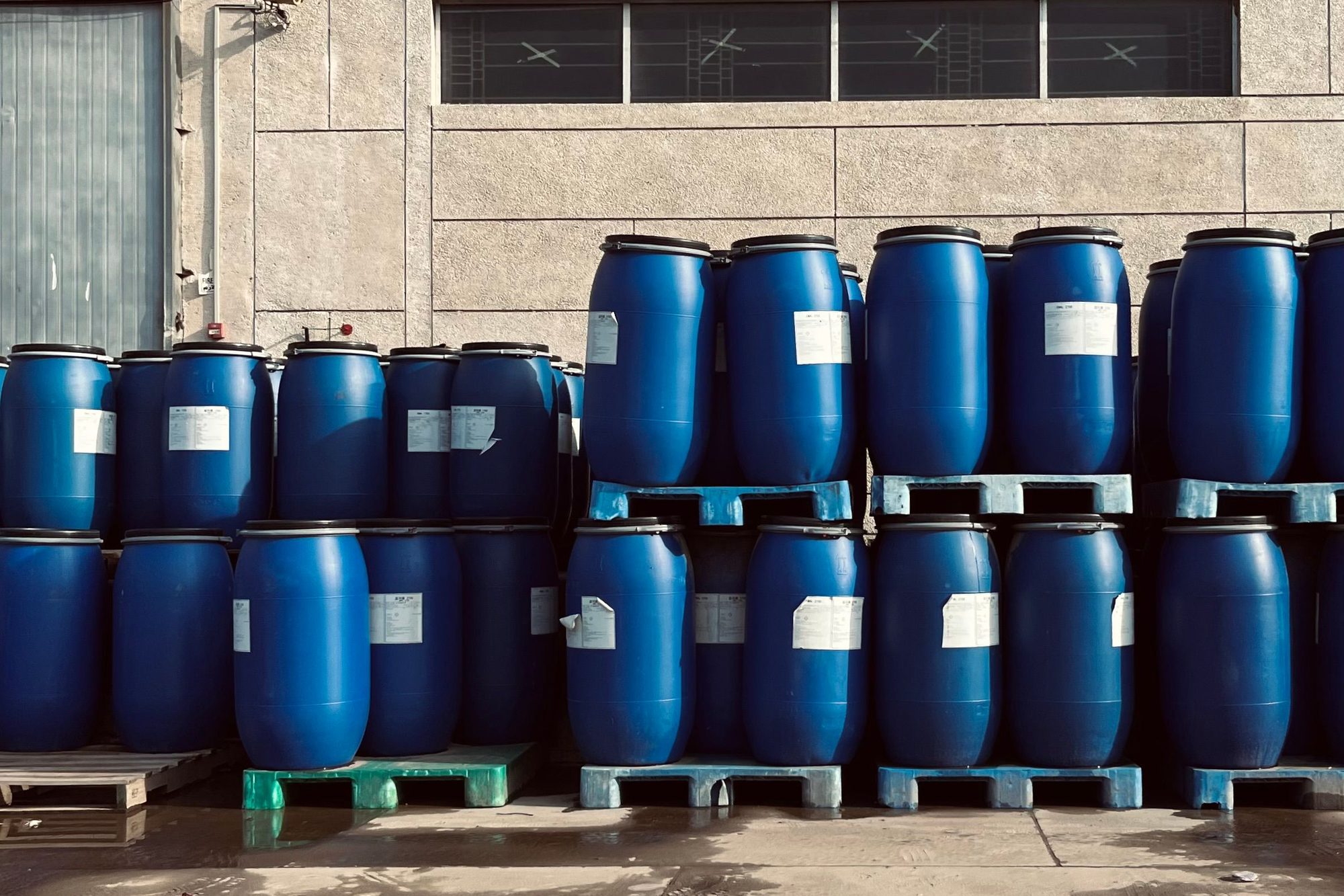 Blue chemical drums stacked on pallets outside a warehouse