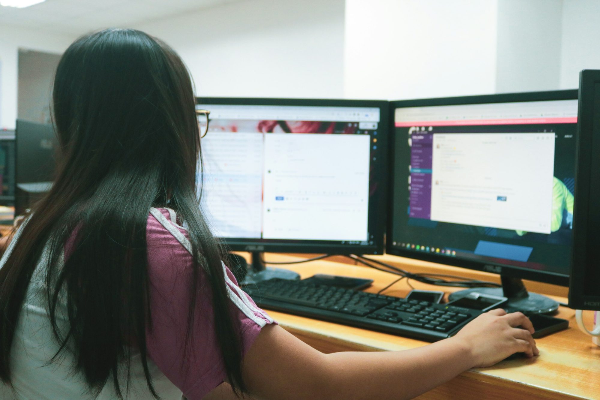 An office worker at a desk with two monitors, seen from behind