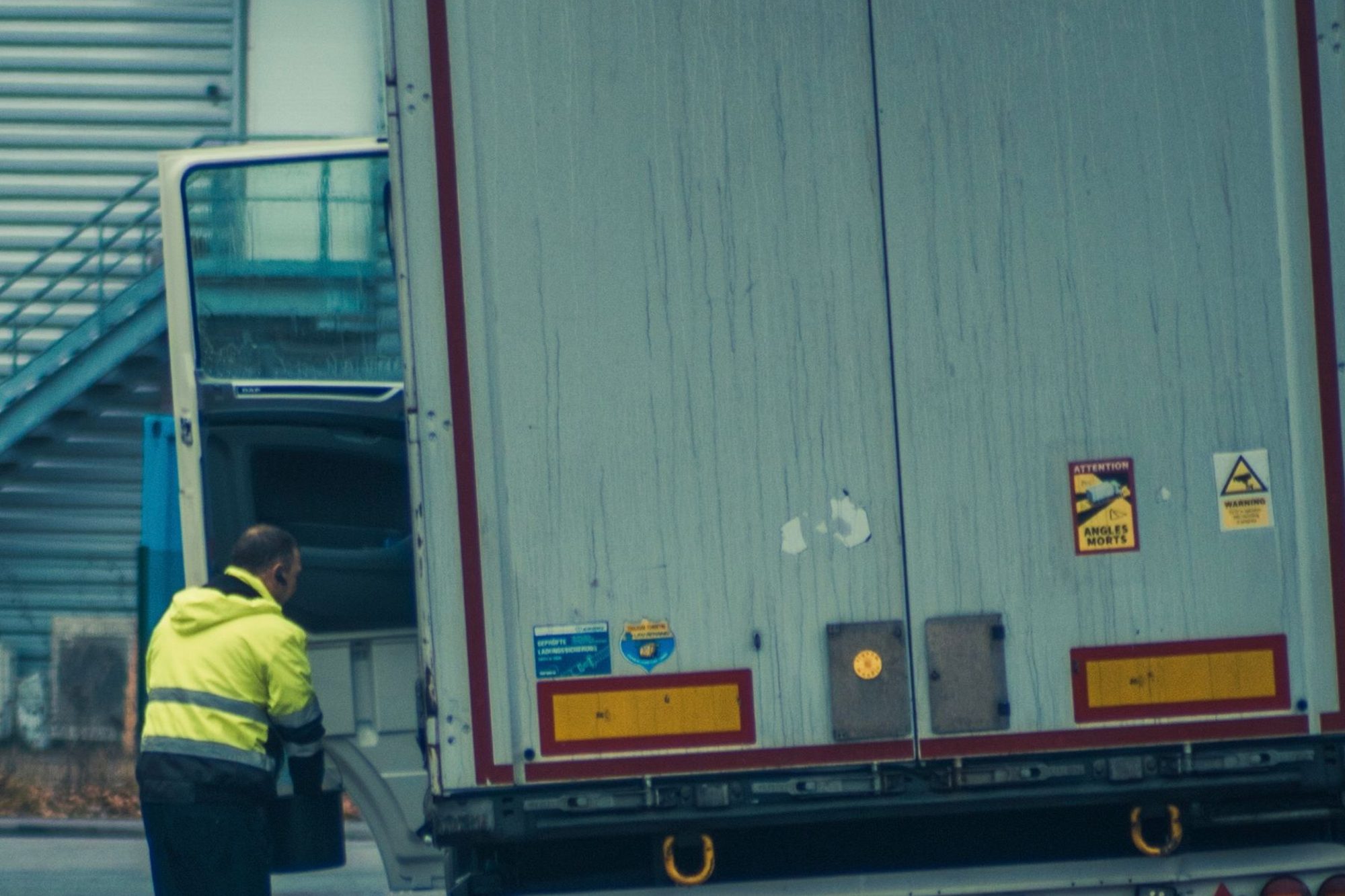 A driver in a high-visibility jacket at the rear doors of a semi trailer